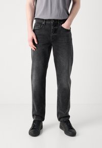 Jeans de mezclilla negra con un ajuste relajado, acabado desgastado, diseño clásico de cinco bolsillos y detalles de costura sutiles. Combinados con zapatillas negras.