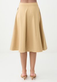Une jupe A-line légère, de longueur genou, en coton beige avec une texture lisse, dotée de poches latérales et d'une fermeture éclair cachée à l'arrière.