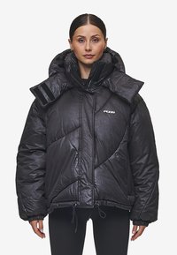 Μαύρο φουσκωτό μπουφάν με ψηλό γιακά, υπερμεγέθες σχέδιο και διαγώνιες ραφές. Διαθέτει ρυθμιζόμενα κορδόνια και λεπτομέρειες από βέλκρο.