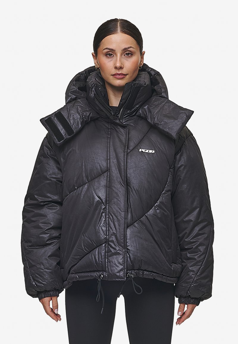 Μαύρο φουσκωτό μπουφάν με ψηλό γιακά, υπερμεγέθες σχέδιο και διαγώνιες ραφές. Διαθέτει ρυθμιζόμενα κορδόνια και λεπτομέρειες από βέλκρο.