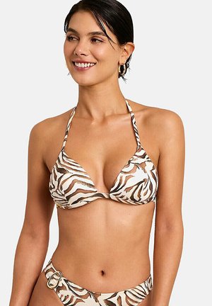 Femme portant un bikini à rayures zèbre marron et blanc avec un haut dos nu et un détail de ceinture sur le bas, souriante et regardant sur le côté.