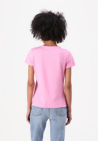 T-shirt rosa a maniche corte con scollatura rotonda, realizzato in soffice tessuto di cotone, indossato da una persona vista di spalle.