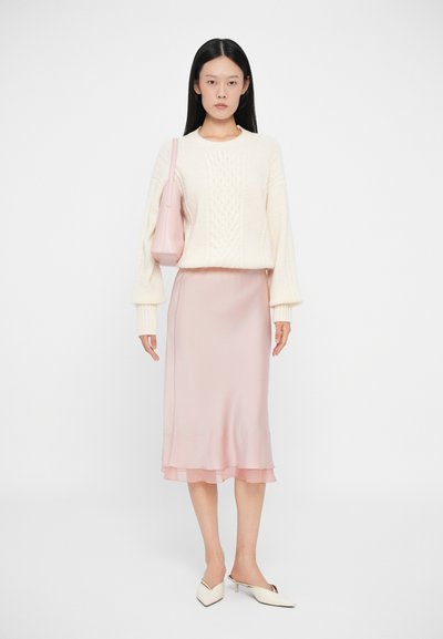 Fehér cable-knit pulóver boleró ujjakkal, világos rózsaszín selyem midi szoknya réteges szegéllyel, és világos rózsaszín táska. Hegyes orrú mamuszok.