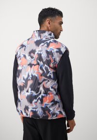 Krāsains, polsterēts bezrūpju vestes modelis ar spirālveida rakstu rozā, zilā un melnā krāsā. Piedāvā augstu apkakli un kontrastējošas piedurknes papildu siltumam.