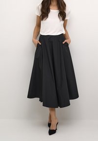 Svart, knälång kjol med en flödande silhuett och sidofickor, kombinerad med en vit t-shirt med kort ärm och svarta klackar.