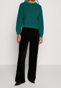 Miętowy prążkowany sweter z długimi rękawami w połączeniu z czarnymi welurowymi spodniami o szerokich nogawkach. Strój ma swobodną, miękką fakturę i nowoczesny krój.