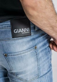 Traperice u svijetloplavoj boji s glatkom teksturom, pet džepova i crnom kožnom etiketom koja glasi "Gianni Kavanagh."