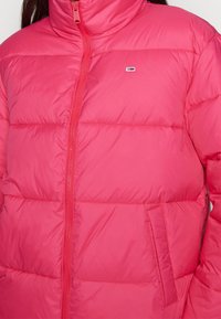 Růžová zimní bunda s vysokým límcem, zipovým uzavřením, bočními kapsami a horizontálním prošíváním. Lehký materiál s hladkou texturou.