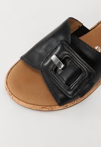 Sandale à bout ouvert avec une sangle en cuir noir dotée d'une grande boucle carrée cousue et d'une semelle intérieure rembourrée beige avec un bord en liège.