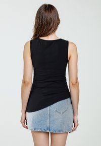 Zwarte mouwloze top van ribstof, gecombineerd met een lichtblauwe denim minirok. De top loopt smal toe bij de taille met een afgeronde zoom.