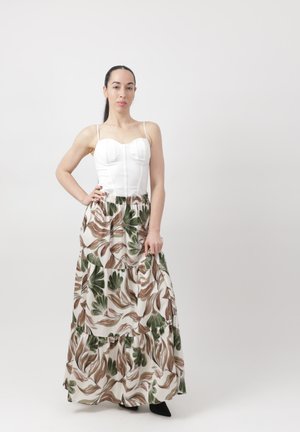 Kobieta o ciemnych włosach, ubrana w biały dopasowany top typu bustier oraz długą, zwiewną spódnicę w zielono-brązowy wzór liści, stojąca na jednolitym białym tle.