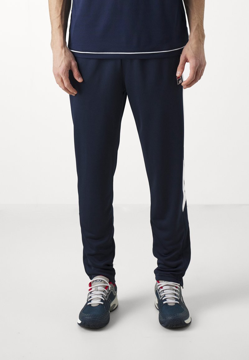 Marineblaue Jogginghosen aus glattem Stoff mit schmalem Schnitt und weißen Seitenakzenten, kombiniert mit grauen und roten sportschuhen.