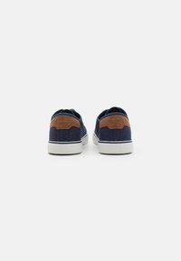 Marineblaue Leinenschuhe mit braunen Wildlederakzenten, weißen Gummisohlen und einem gerundeten Rückendesign. Texturiert für Atmungsaktivität.