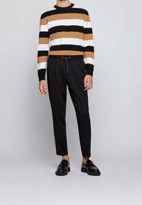 Pull rayé avec des bandes horizontales marron, blanches et noires ; associé à un pantalon noir sur mesure avec une taille à cordon et une ceinture.
