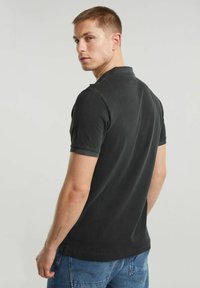 Polo shirt nera a maniche corte, in tessuto texturizzato, con colletto classico e orlo dritto, abbinata a jeans blu.