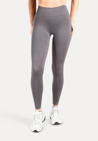 Leggings grigie realizzate in materiale liscio ed elastico, con vita alta e design aderente, abbinate a sneakers bianche.