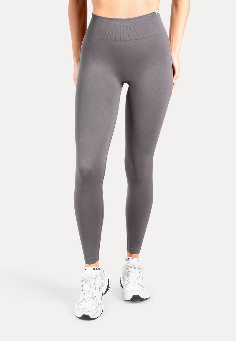 Leggings grigie realizzate in materiale liscio ed elastico, con vita alta e design aderente, abbinate a sneakers bianche.