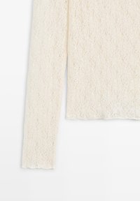 Langärmliges, cremefarbenes Oberteil mit strukturiertem, offen gestricktem Spitzenmuster und wellenförmigem Saumdetail.