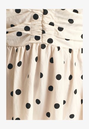 Vestito in cotone color crema con corpetto arricciato e gonna svasata, decorato con grandi pois neri su tutta la superficie. Tessuto morbido.