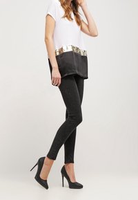 Svarte tætsiddende jeans parret med en hvid top, der har en sort satin-nederdel og en guld pailletbånd, båret med sorte højhælede sko.