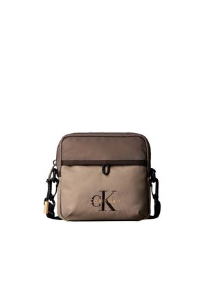 Mała dwukolorowa brązowa torebka Calvin Klein na ramię z przednią kieszenią i regulowanym czarnym paskiem, z logo CK i nazwą marki.