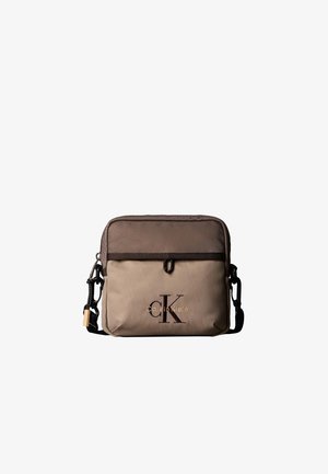 Mała dwukolorowa brązowa torebka Calvin Klein na ramię z przednią kieszenią i regulowanym czarnym paskiem, z logo CK i nazwą marki.