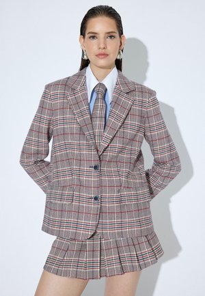 Geruite blazer in beige met rode en groene accenten, voorzien van brede revers en twee knopen, gecombineerd met een bijpassende geplooide minirok.