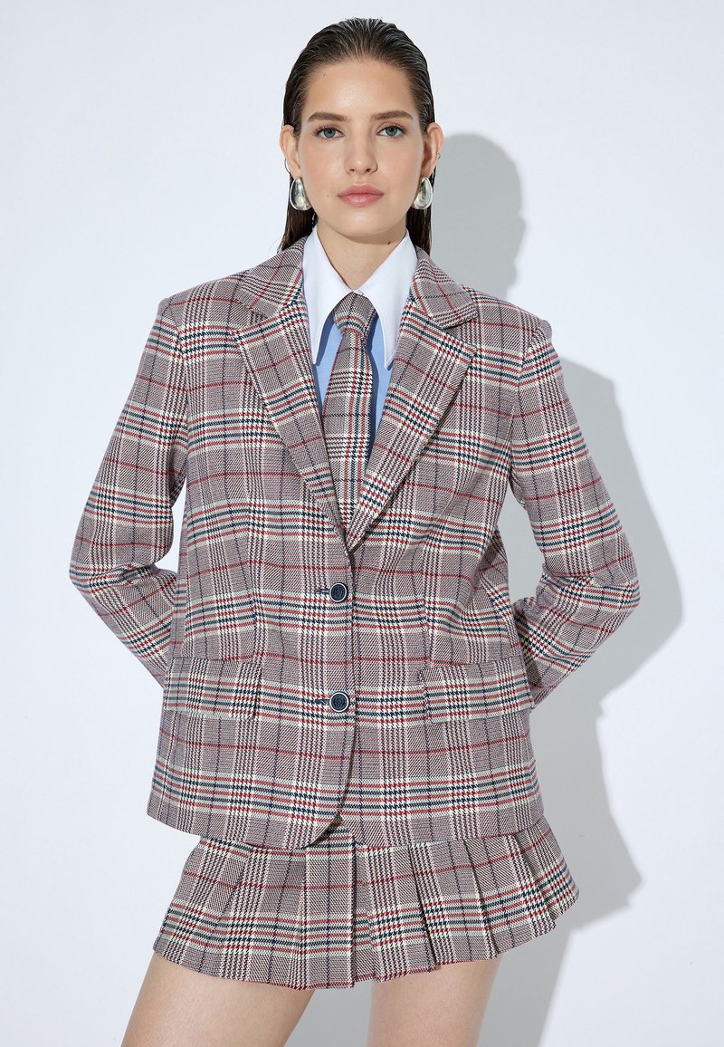 Geruite blazer in beige met rode en groene accenten, voorzien van brede revers en twee knopen, gecombineerd met een bijpassende geplooide minirok.