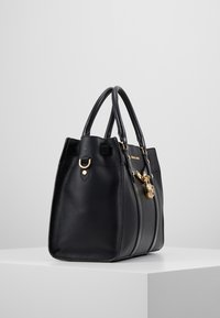 Borsa a tracolla in pelle nera con texture granulosa, con accenti in hardware dorato e manici doppi; presenta un dettaglio con lucchetto sul davanti.