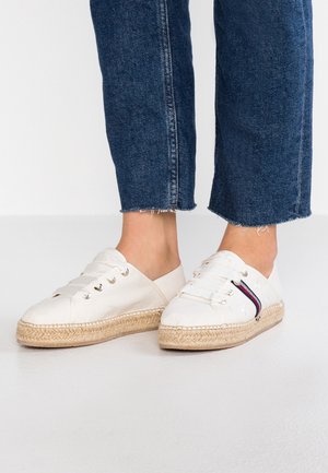 Białe płócienne buty espadryle z grubymi białymi sznurówkami, jutyowymi podeszwami i wzorem gwiazdek, noszone z niebieskimi jeansami o krótkiej długości.