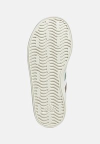 Semelle de sneaker en caoutchouc blanc avec des motifs en vagues, présentant un léger talon et trois rayures colorées. Logo embossé sur le côté.