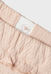 Blassrosa gestrickter Bund mit gerippter Textur und weichem Elastik. Verfügt über einen weißen Stoffstreifen und einen transparenten Knopf zum Schließen.