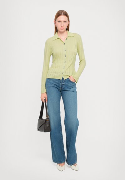 Light green ribbed knit cardigan with button closure, paired with blue wide-leg jeans. Black handbag and white pointed-toe shoes.