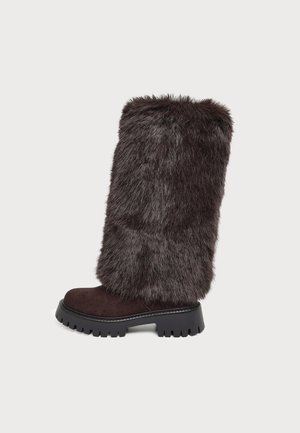 Botte marron foncé montant jusqu’au genou, avec une tige épaisse en fourrure, un pied en daim et une semelle noire épaisse à crampons.