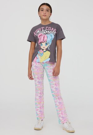 T-shirt grigia con stampa di cartone animato colorata raffigurante una ragazza che tiene un gelato, abbinata a jeans con motivo tie-dye pastello. Sneakers bianche.