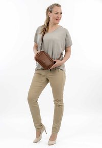 Borsa a tracolla beige con accenti intrecciati, indossata con un top grigio loose e pantaloni fit beige, abbinata a scarpe con tacco nude.