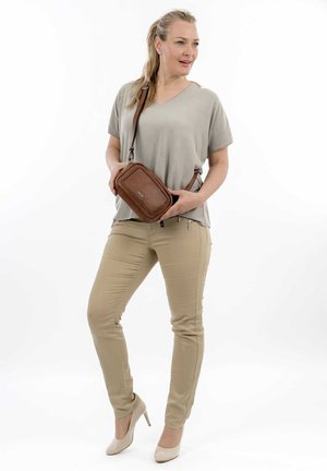 Borsa a tracolla beige con accenti intrecciati, indossata con un top grigio loose e pantaloni fit beige, abbinata a scarpe con tacco nude.