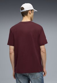 Bordeaux kortærmet T-shirt lavet af bomuld. Rund hals design med en afslappet pasform. Bæres med lyseblå denimjeans. Hvid kasket synlig.