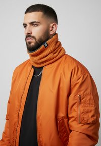 Orange bomber jacket with zip closure and side pocket, paired with an orange chunky knit neck warmer featuring a black label.