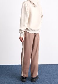 Ljust beige hoodie med en mjuk textur, parat med lösa bruna sweatpants med vita sidlinien och svarta klumpiga skor.