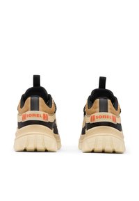 Baskets noir et marron avec une semelle épaisse crème, arborant un logo orange "SOREL" et des détails texturés sur la tige pour une meilleure adhérence.