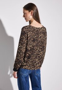 Leopardikuosi neule ruskeassa ja mustassa, ylisuuri malli pitkillä hihoilla, pyöreällä kaula-aukolla ja ribbauslahkeilla, yhdistettynä sinisiin farkkuihin.