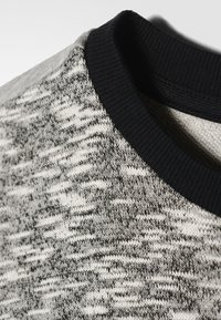 Maglione lavorato a maglia grigio e nero con scollo rotondo, caratterizzato da un motivo testurizzato e un bordo a coste nero sul collo.