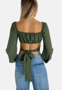 Top corto verde oliva con maniche a sbuffo, dotato di scollatura quadrata e dettaglio legato sul retro. Abbinato a jeans di denim strappati a vita alta.