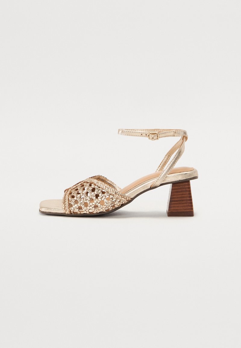 Sandale dorée à bout ouvert avec bride avant tressée, bride de cheville avec boucle et talon bloc en bois empilé et épais.