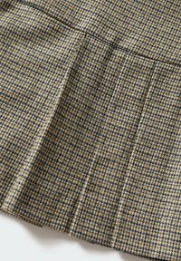 Tissu en tweed avec un petit motif pied-de-poule noir, blanc et marron, présentant un détail de pli avant.