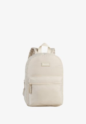 Beige backpack with rounded shape, made of durable fabric, featuring a front zip pocket and adjustable straps. Brand logo is displayed on the front.