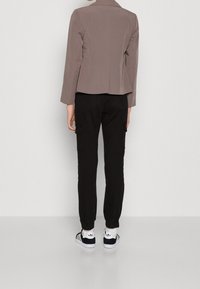 Brun skräddarsydd jacka med en figursydd design, tillsammans med svarta cargobyxor och svart-vita sneakers. Slät textur och strukturerad silhuett.