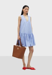 Light blue striped sleeveless dress with a V-neck and flared hem. Paired with a brown tote bag and red mules.