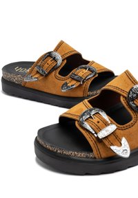 Sandales en daim marron avec deux boucles en métal argenté, design ouvert, semelle noire texturée et surpiqûres contrastées. Elles présentent un détail en liège sur la semelle.